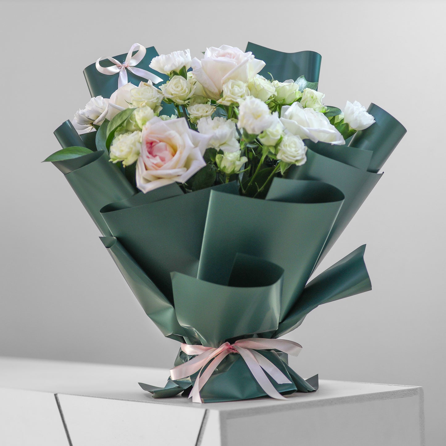 Luxury bouquet of O’Hara roses, white carnations, and miniature roses wrapped in green paper with a pink ribbon