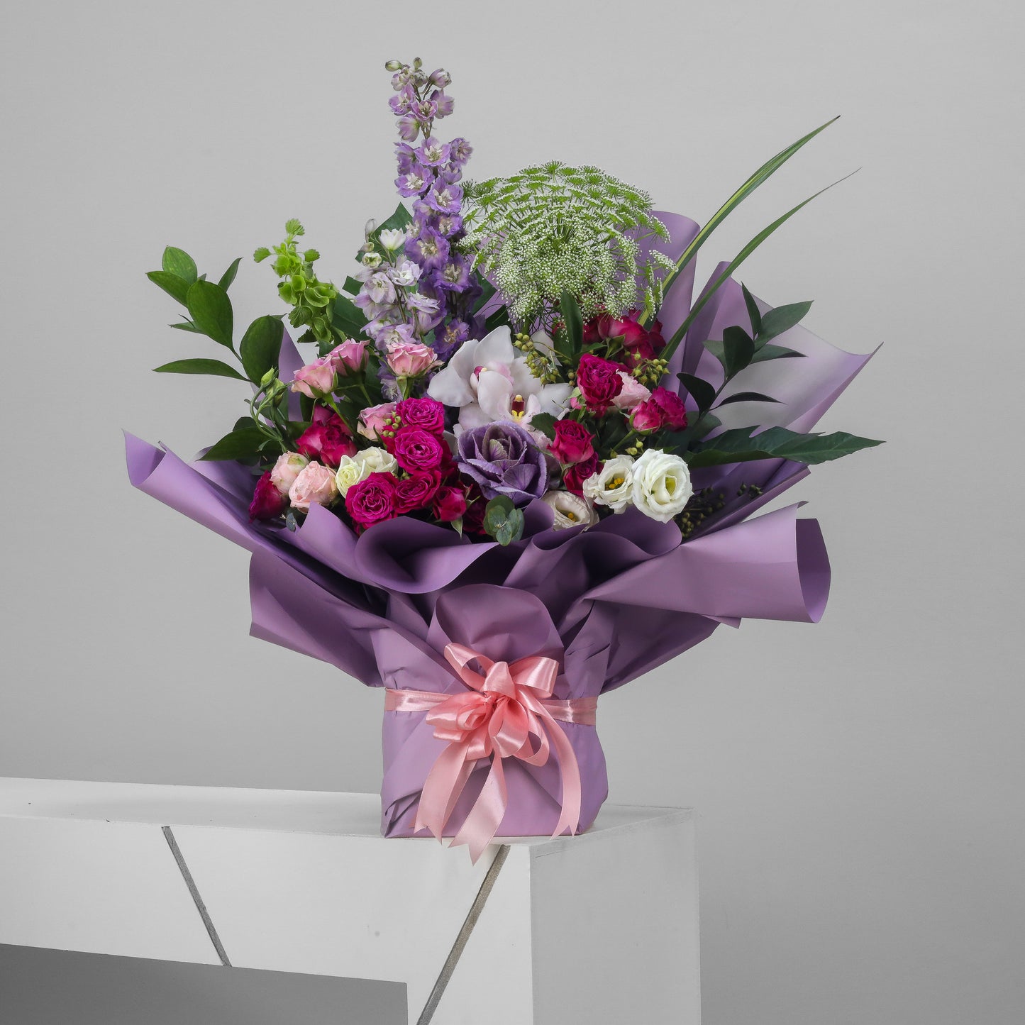Elegant mixed bouquet with roses, lisianthus, and purple flowers wrapped in lavender paper and peach ribbon – luxury floral arrangement