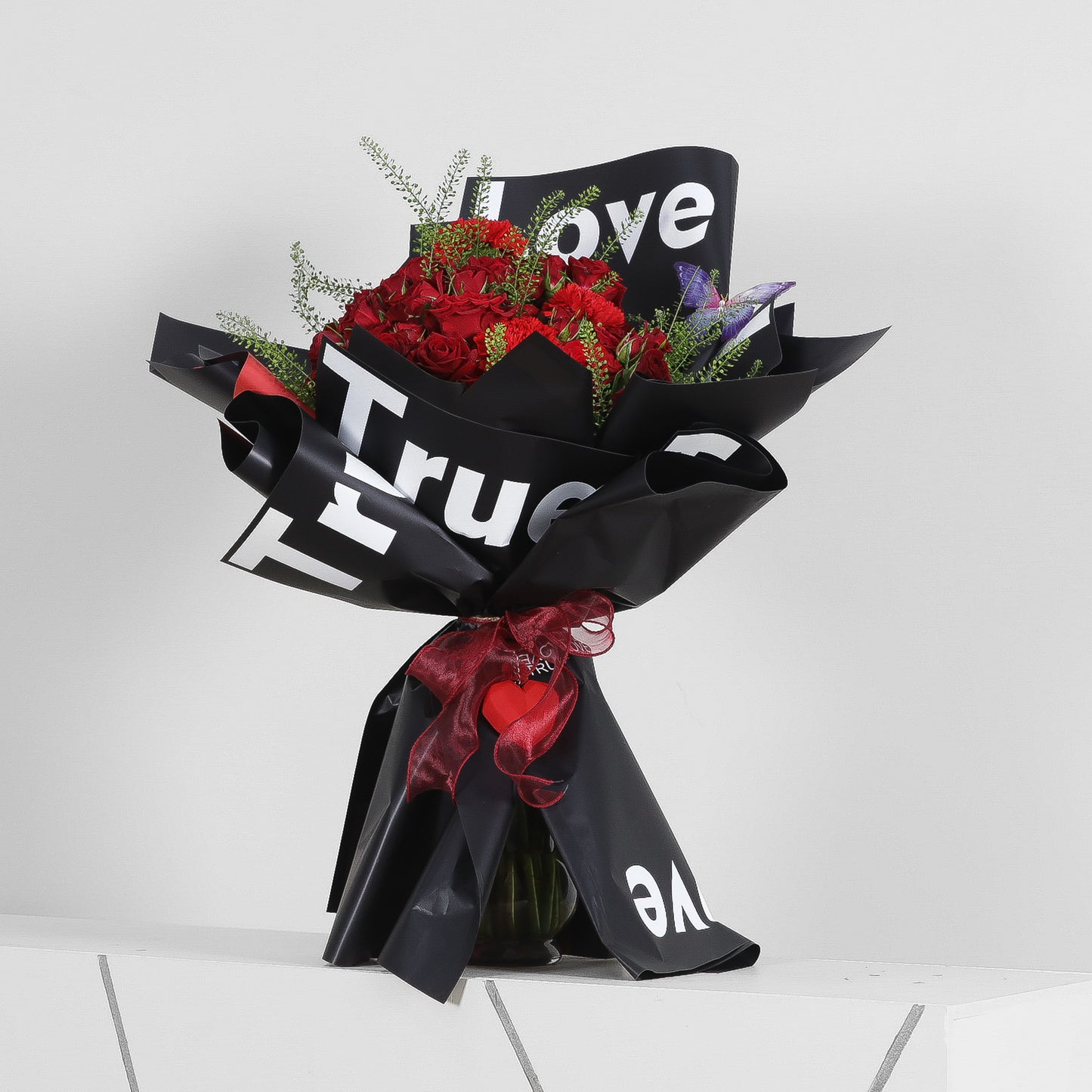 Luxurious red rose bouquet with purple fillers in black “True Love” wrapping and red heart ribbon – romantic floral gift